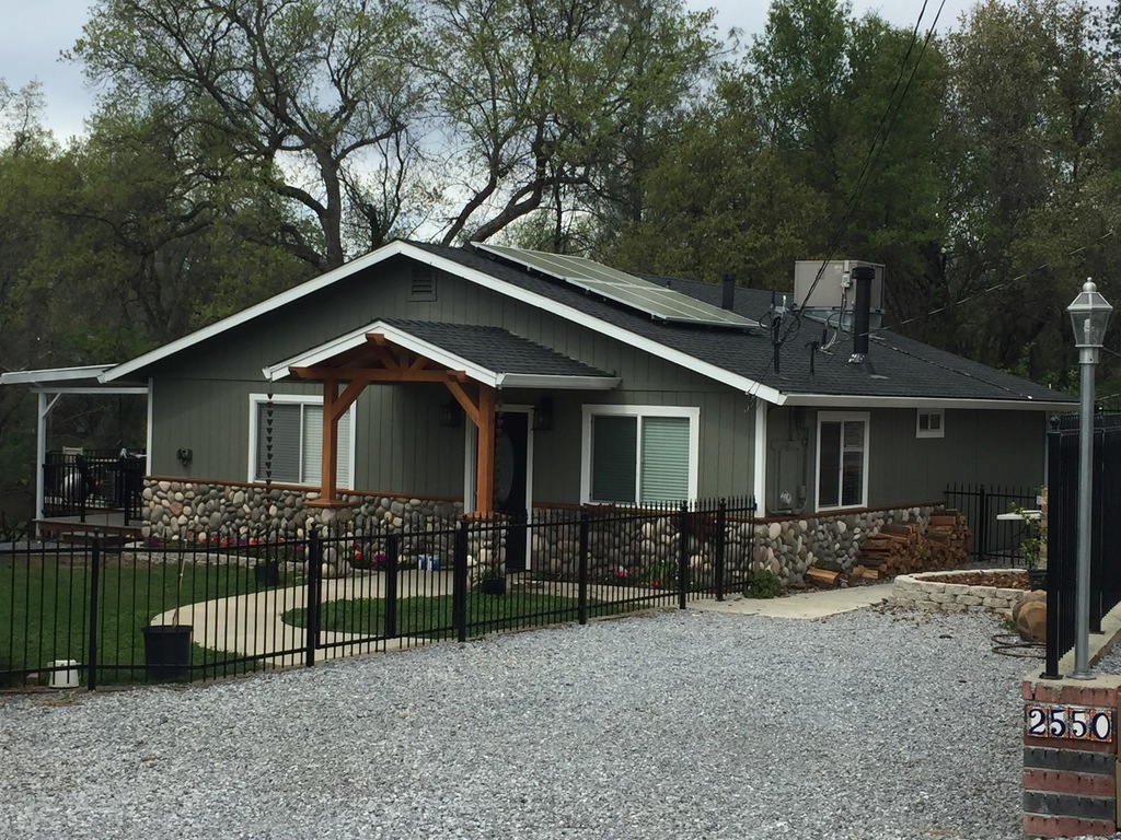 Gray board and batten home with river rock wainscot and black iron fence, exterior painted in Redding California