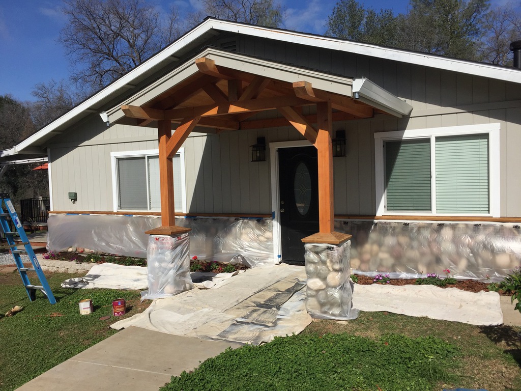 Exterior painting prep in Redding with stone pillars and landscaping fully masked in plastic before spraying