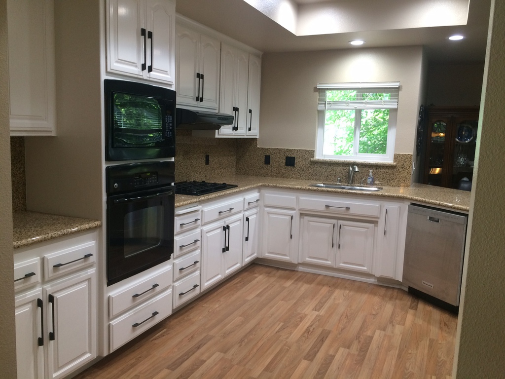 Kitchen cabinets refinished from oak to white by Talbot Painting in Redding, with wood floors and granite backsplash